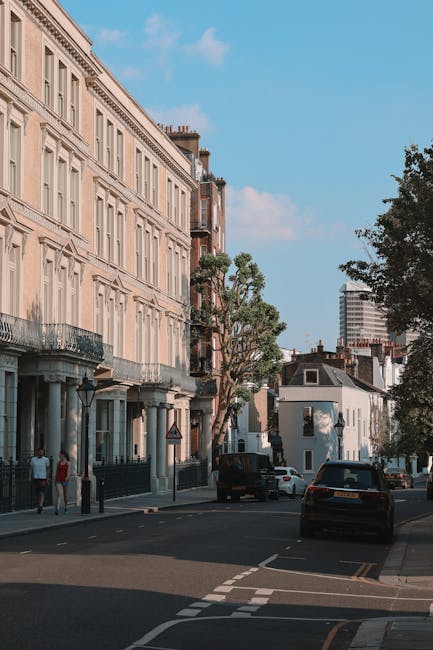 A red double-decker bus driver is stopped at a bus lane on a busy street in Maida Vale, London, with historic red-brick residential buildings featuring bay windows and decorative cornices lining the background. The bus, displaying route number 414, is positioned near the curb, with trees casting shade across the scene and traffic cones placed nearby to manage vehicle flow. The environment appears bright and clear, with sunlight illuminating the scene. This setting depicts typical urban transit and transportation elements that could be associated with house removals or logistics planning in the Maida Vale area, supporting services like furniture transport, packing, and loading during home relocation processes. Man and a Van Maida Vale, a company specializing in removals, may use such routes for efficient movement of household items between properties.