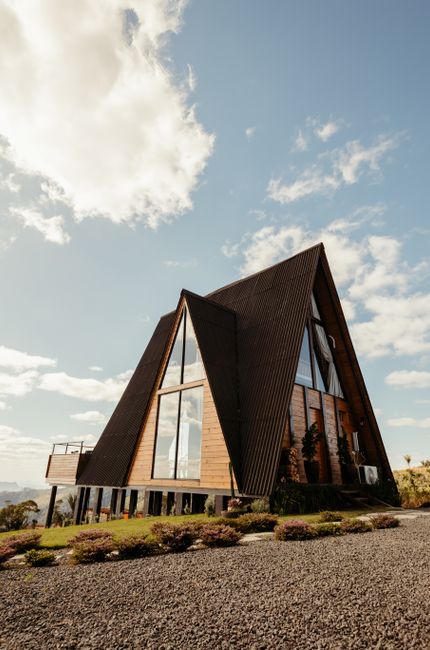 A row of multi-storey residential buildings with a mix of brick and white-painted facades viewed from the street on a clear, sunny day. The buildings feature traditional sash windows and external fire escape staircases made of black metal that zigzag along the front facades. A black street lamp with a glass lantern is positioned on the pavement in front of the buildings, casting shadows on the white wall below. There is a small garden area with green foliage hanging over a white boundary wall at the ground level, adjacent to the buildings. The sky is a vibrant blue with no clouds, emphasizing the bright and sunny weather. The scene captures the typical architecture of Maida Vale, suitable for home relocation and furniture transport activities, with exterior features that may be part of a building clearance or moving process.